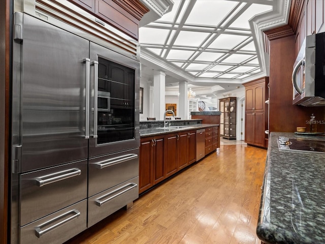 kitchen featuring stainless steel appliances, coffered ceiling, dark stone countertops, sink, and light hardwood / wood-style flooring