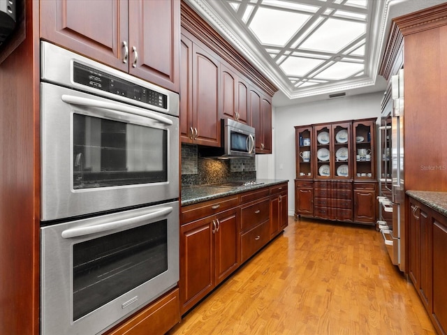 kitchen featuring appliances with stainless steel finishes, backsplash, light hardwood / wood-style flooring, and dark stone counters