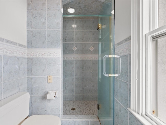 bathroom with tile walls, toilet, and a shower with shower door