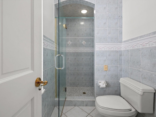 bathroom featuring tile flooring, a shower with shower door, toilet, and tile walls