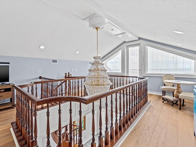 corridor with lofted ceiling, light hardwood / wood-style flooring, and a textured ceiling