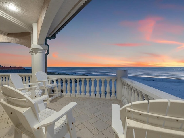 balcony at dusk featuring a water view