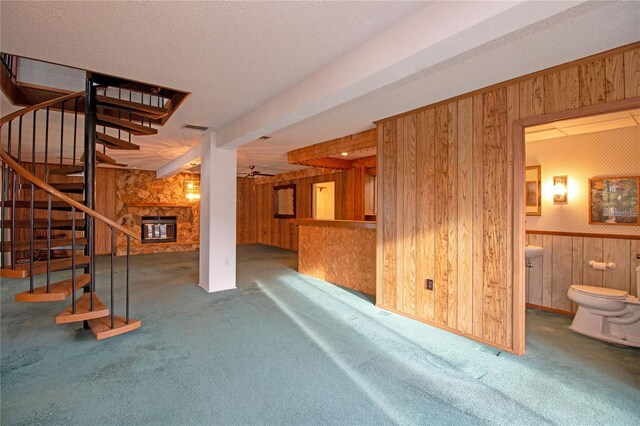 carpeted living room featuring a fireplace, wooden walls, a textured ceiling, and indoor bar