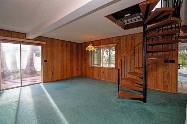 unfurnished living room with beamed ceiling, dark carpet, a textured ceiling, and wooden walls