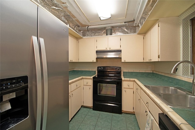 kitchen with light tile patterned floors, sink, stainless steel fridge, black range with electric cooktop, and cream cabinetry