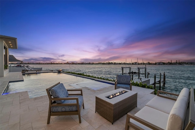 patio terrace at dusk featuring a dock, a water view, and an outdoor living space with a fire pit