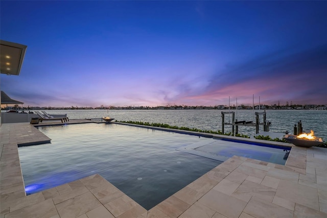 pool at dusk featuring an outdoor fire pit, a water view, and a boat dock