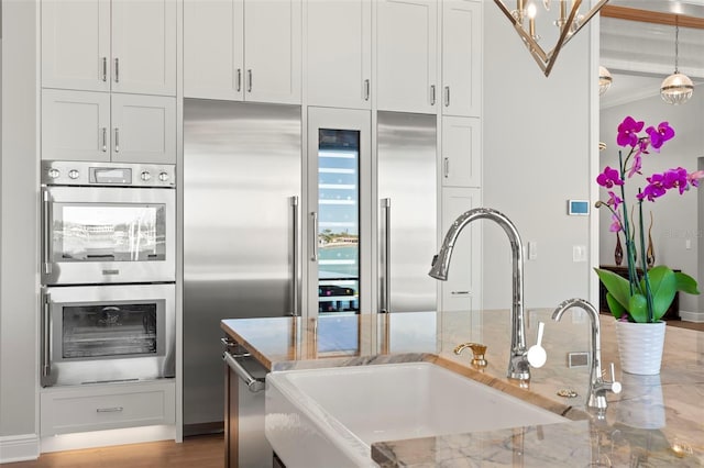 kitchen featuring hanging light fixtures, sink, white cabinetry, light stone countertops, and stainless steel double oven