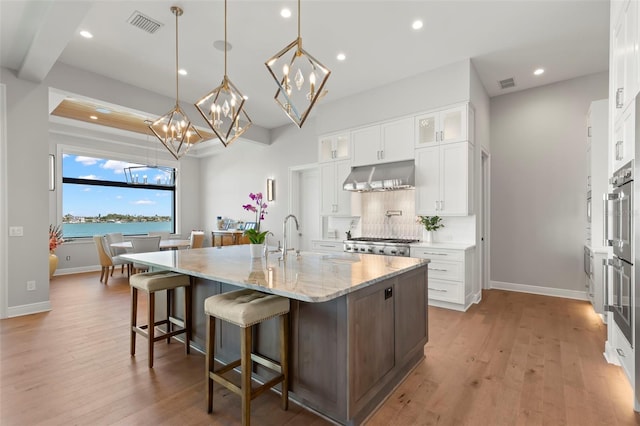 kitchen featuring hanging light fixtures, white cabinets, a water view, light stone countertops, and a center island with sink