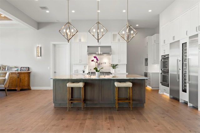 kitchen with white cabinetry, range hood, a kitchen island with sink, pendant lighting, and a breakfast bar area