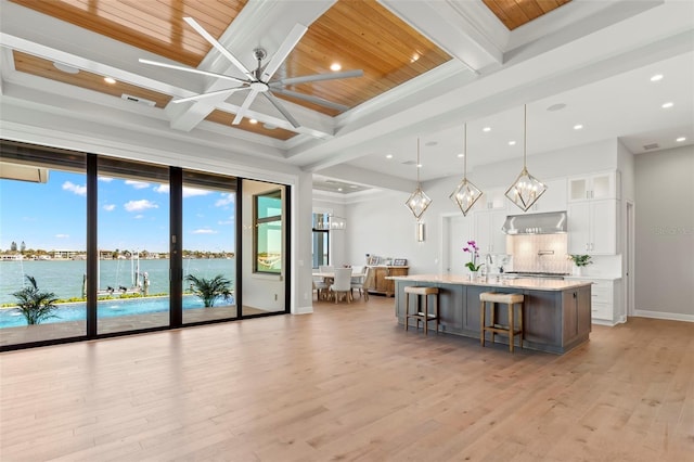 kitchen with decorative light fixtures, white cabinets, a water view, beam ceiling, and a large island with sink