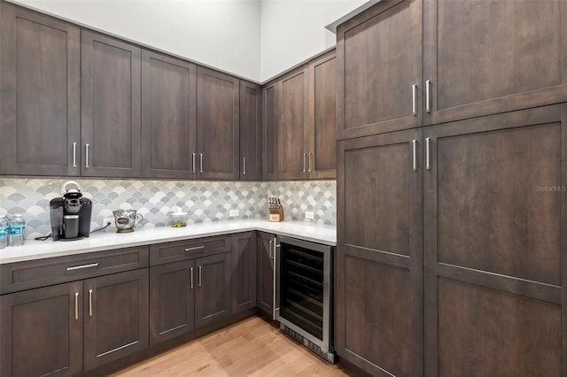 kitchen featuring backsplash, dark brown cabinetry, light hardwood / wood-style flooring, and wine cooler