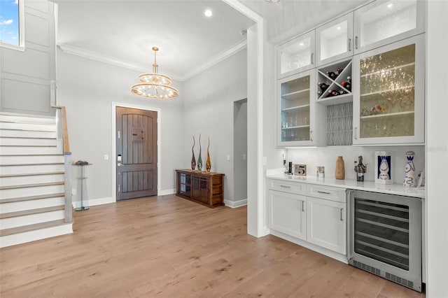 bar featuring white cabinetry, wine cooler, light hardwood / wood-style floors, hanging light fixtures, and crown molding