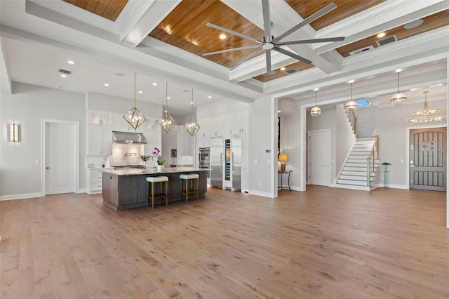 kitchen with a large island with sink, white cabinets, pendant lighting, and beam ceiling