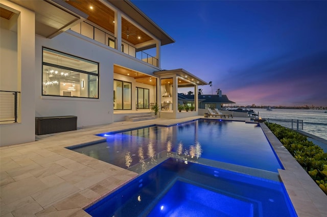 pool at dusk featuring an in ground hot tub, a water view, and a patio area