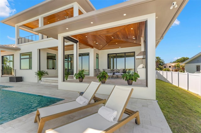 rear view of property featuring a balcony, a fenced in pool, a patio area, and a lawn