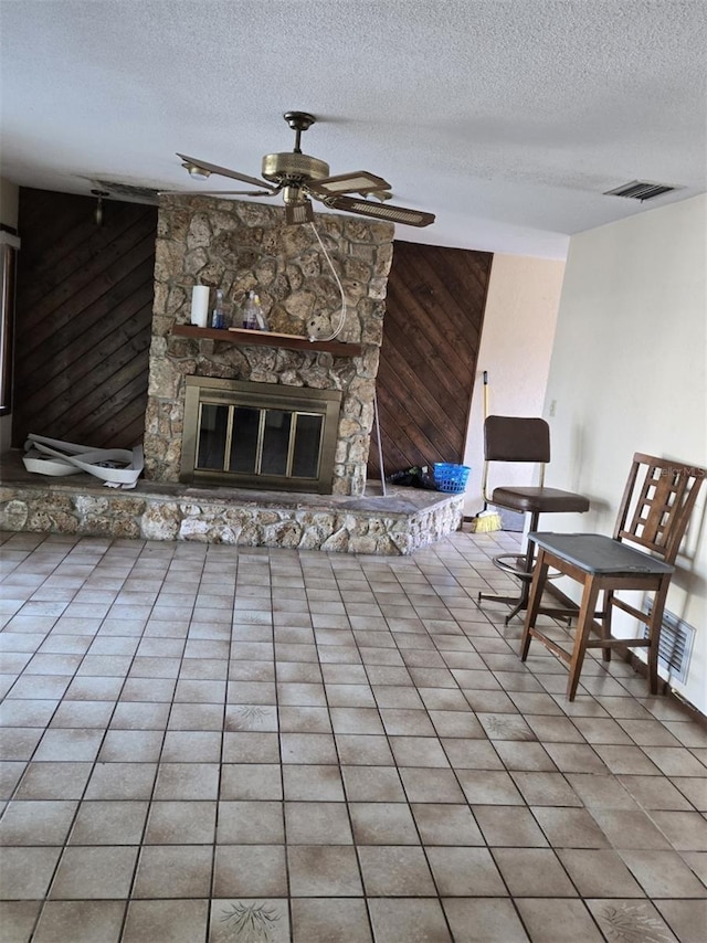 tiled living room with a stone fireplace, wood walls, a textured ceiling, and ceiling fan