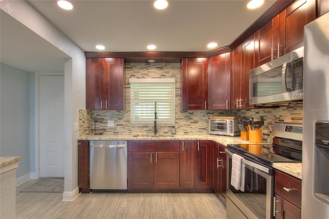 kitchen featuring light stone countertops, decorative backsplash, stainless steel appliances, sink, and light hardwood / wood-style floors