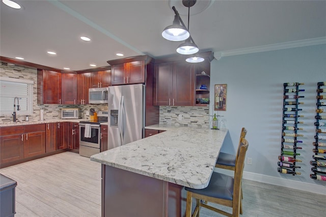 kitchen featuring hanging light fixtures, ornamental molding, appliances with stainless steel finishes, a kitchen bar, and kitchen peninsula