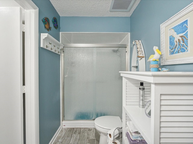 bathroom featuring a textured ceiling, hardwood / wood-style flooring, a shower with shower door, and toilet