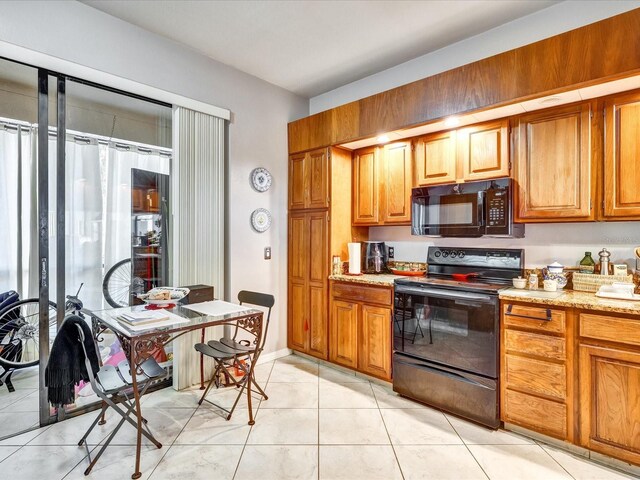 kitchen with light tile floors, light stone countertops, and black appliances