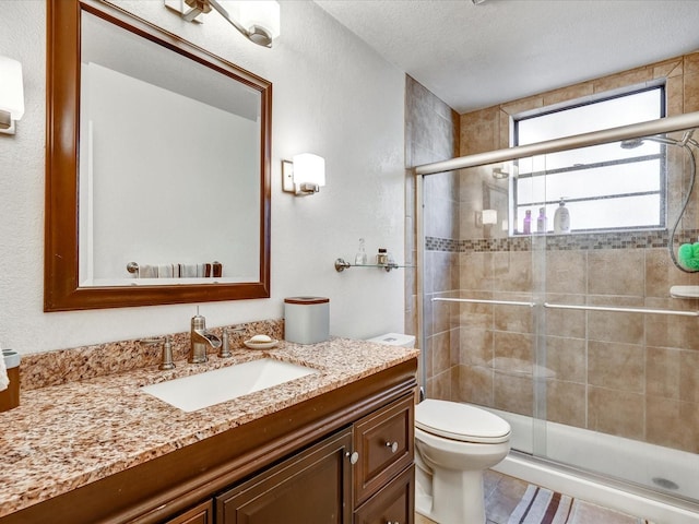 bathroom with toilet, a shower with shower door, a textured ceiling, vanity, and tile flooring