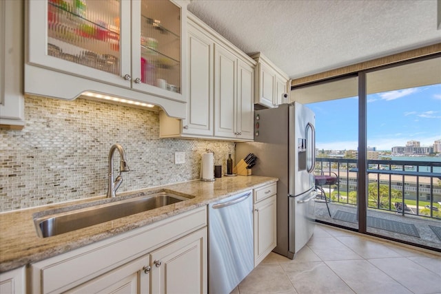 kitchen featuring sink, light stone counters, backsplash, stainless steel appliances, and a textured ceiling