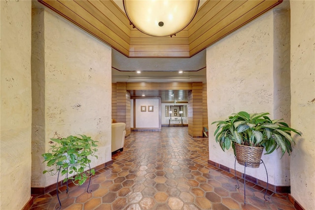 interior space featuring dark tile floors, ornamental molding, wood ceiling, and a raised ceiling