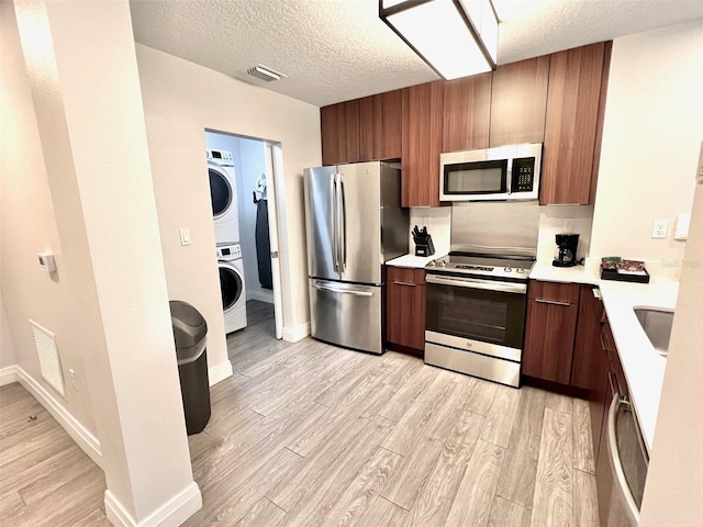 kitchen with sink, stacked washer and dryer, light hardwood / wood-style floors, a textured ceiling, and appliances with stainless steel finishes