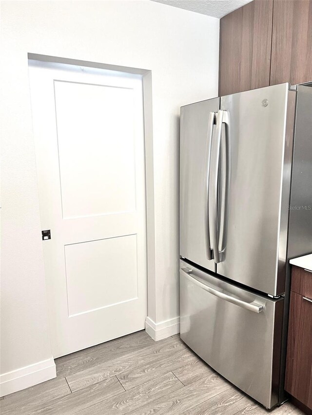 kitchen with dark brown cabinets, light wood-type flooring, and stainless steel refrigerator