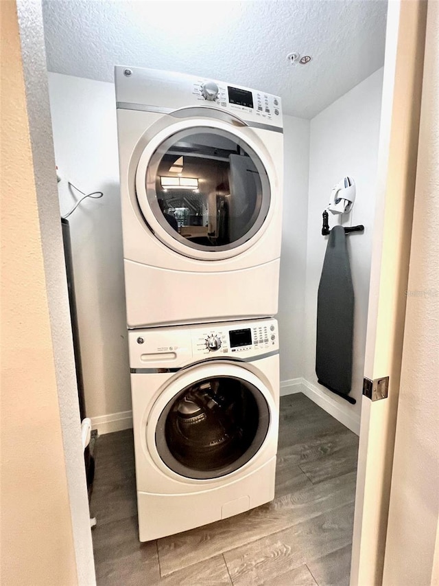 laundry room featuring hardwood / wood-style floors, a textured ceiling, and stacked washing maching and dryer