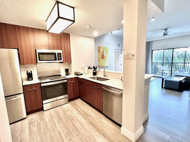 kitchen featuring ceiling fan, sink, stainless steel appliances, a textured ceiling, and light wood-type flooring