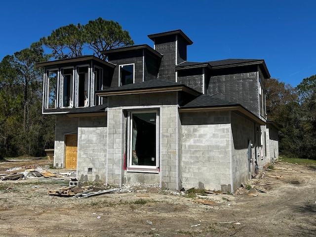 rear view of house with concrete block siding, roof with shingles, and a chimney