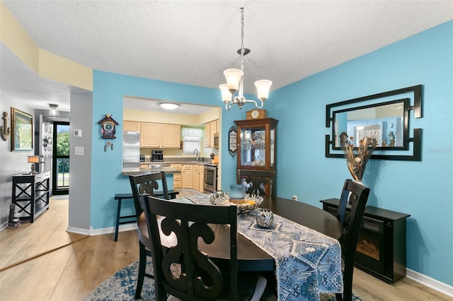 dining room with sink, a notable chandelier, light wood-type flooring, and a textured ceiling