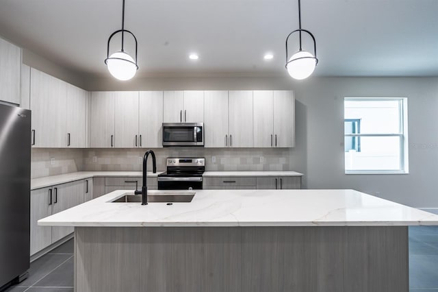 kitchen featuring appliances with stainless steel finishes, hanging light fixtures, an island with sink, light stone counters, and sink