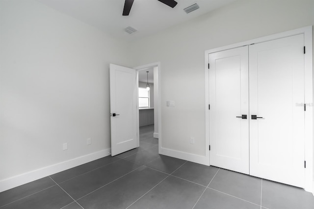 unfurnished bedroom with a closet, dark tile flooring, and ceiling fan