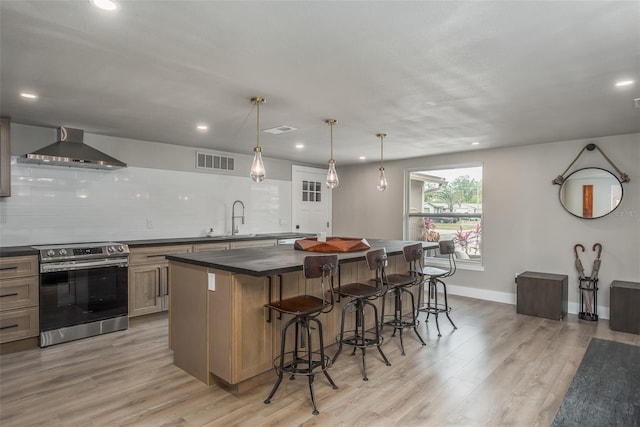 kitchen featuring wall chimney exhaust hood, a kitchen island, electric stove, light wood-type flooring, and a breakfast bar area