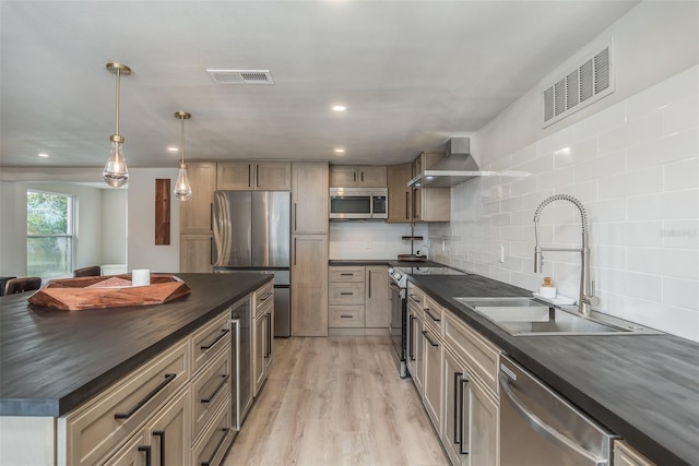 kitchen featuring appliances with stainless steel finishes, backsplash, wall chimney exhaust hood, pendant lighting, and light wood-type flooring