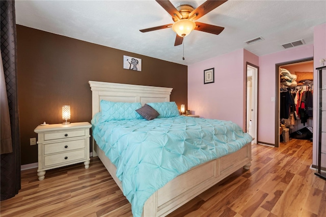 bedroom with a closet, a spacious closet, light hardwood / wood-style floors, and ceiling fan