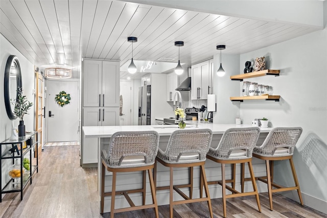 kitchen featuring kitchen peninsula, wall chimney exhaust hood, light wood-type flooring, white cabinetry, and stainless steel appliances