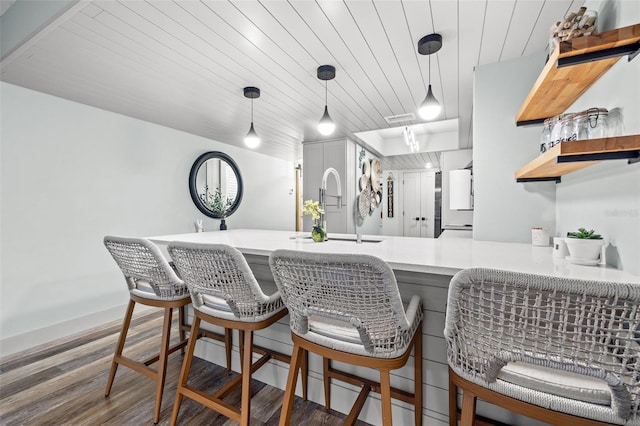 kitchen with a breakfast bar, kitchen peninsula, sink, decorative light fixtures, and wood-type flooring