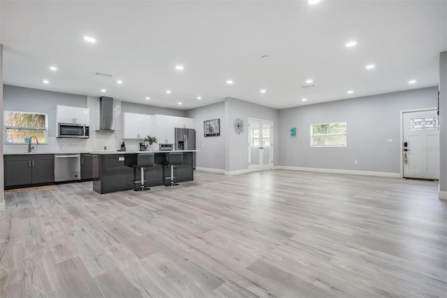 kitchen with wall chimney exhaust hood, white cabinets, a wealth of natural light, stainless steel appliances, and light hardwood / wood-style floors