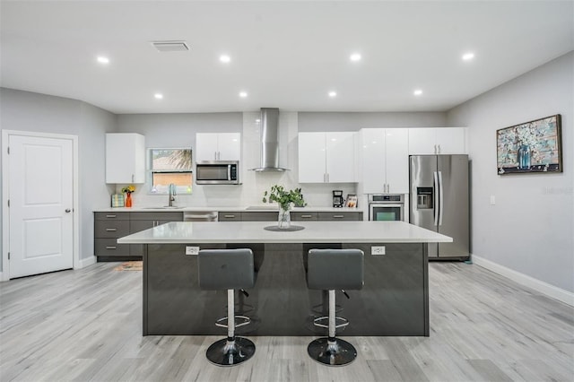 kitchen with appliances with stainless steel finishes, light hardwood / wood-style floors, wall chimney range hood, and white cabinets