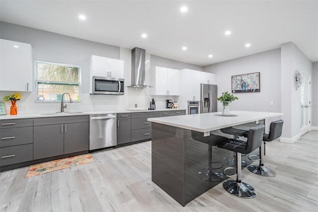 kitchen with wall chimney exhaust hood, white cabinets, sink, a kitchen bar, and stainless steel appliances