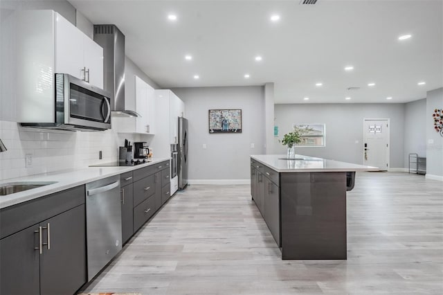 kitchen with appliances with stainless steel finishes, white cabinets, tasteful backsplash, light hardwood / wood-style flooring, and a kitchen breakfast bar