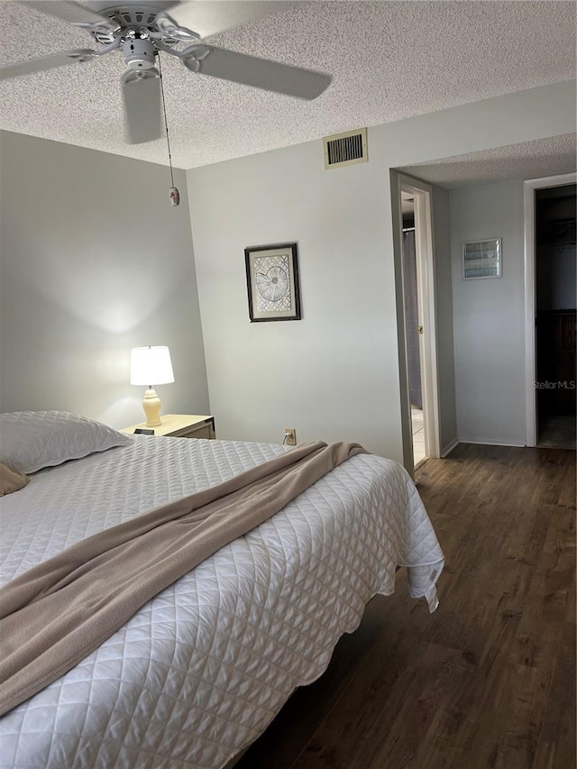 bedroom featuring a ceiling fan, visible vents, a textured ceiling, and wood finished floors