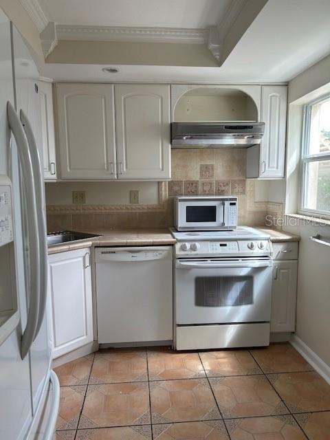 kitchen featuring white cabinets, light tile patterned flooring, white appliances, backsplash, and exhaust hood