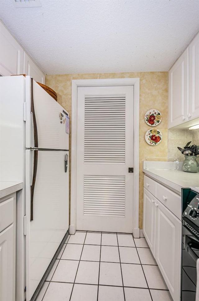 kitchen with stove, light tile floors, white cabinets, and white fridge