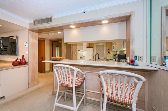 kitchen with white refrigerator, light colored carpet, crown molding, kitchen peninsula, and a textured ceiling