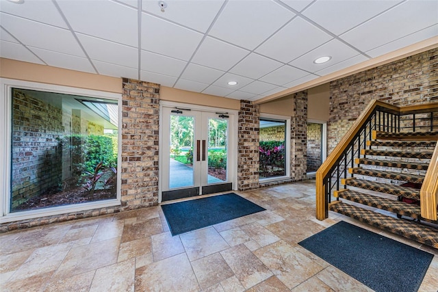 entryway featuring brick wall, a paneled ceiling, light tile floors, and french doors